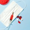 Face mask, syringe, and pills on a blue background, symbolizing healthcare and medical research.