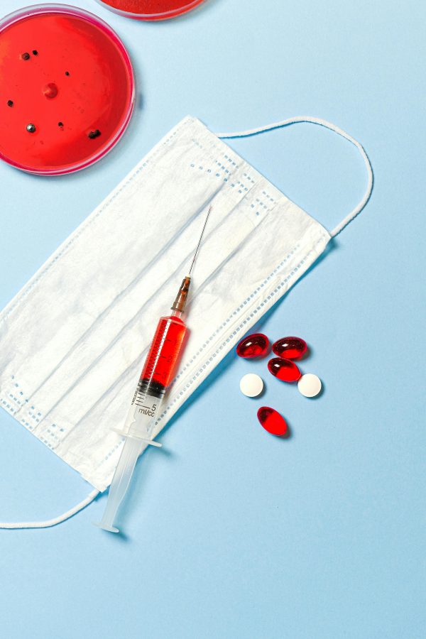 Face mask, syringe, and pills on a blue background, symbolizing healthcare and medical research.