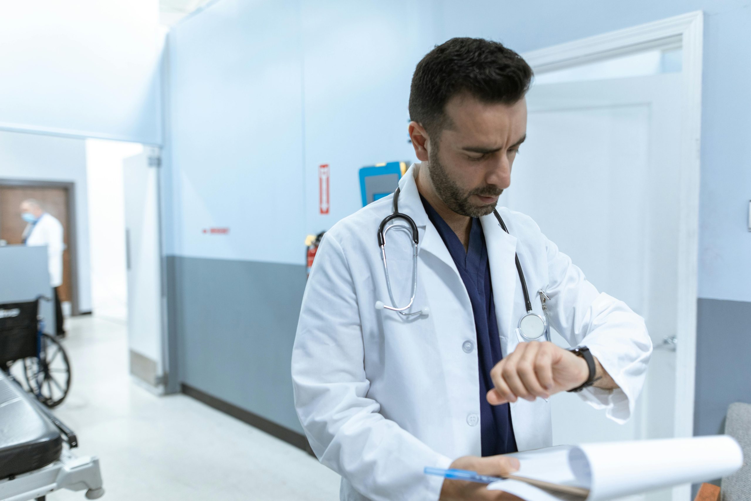 A doctor in a white lab coat checks his wristwatch in a hospital hallway, conveying professionalism.